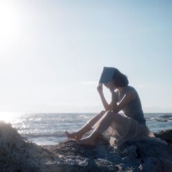 Woman sitting on beach against sky