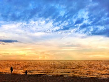 Silhouette people on beach against sky during sunset