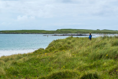 Mid distance on boy standing on grassy lakeshore against sky