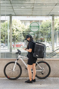 Young female delivery person using mobile phone by bicycle during pandemic