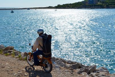 Rear view of man riding motorcycle by sea