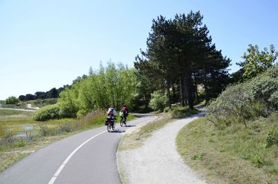 People riding bicycle on road against sky