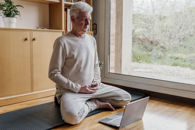 Man learning yoga on laptop at home