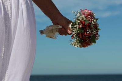 Close-up of hand holding bouquet against sea