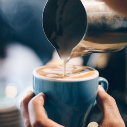 Cropped hand pouring milk in coffee