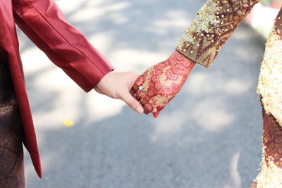 Midsection of bride and groom holding hands on road