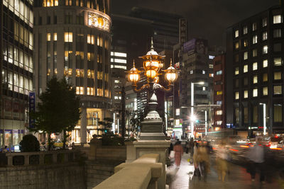 People on illuminated street amidst buildings in city at night