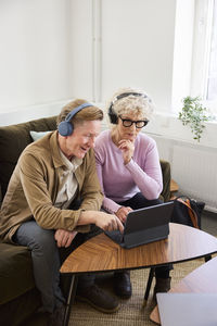 Senior man and woman sitting in living room and using laptop and digital tablet to edit podcast