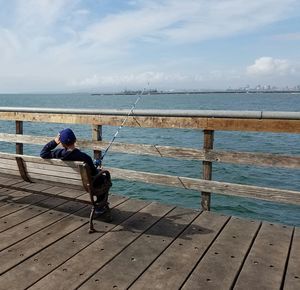 Rear view of man fishing at sea shore against sky