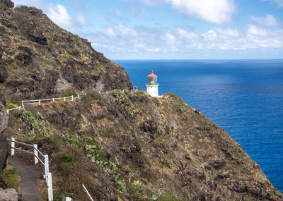 Lighthouse on cliff by sea against sky