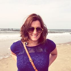 Portrait of young woman wearing sunglasses standing at beach