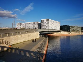 Bridge over river by buildings in city against sky