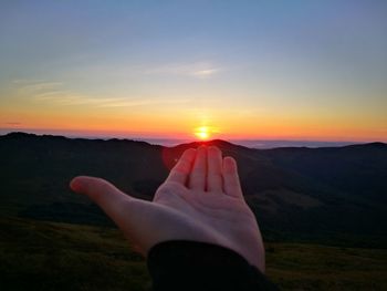 Cropped hand reaching sky during sunset