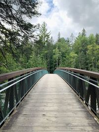 Footbridge amidst trees in forest against sky