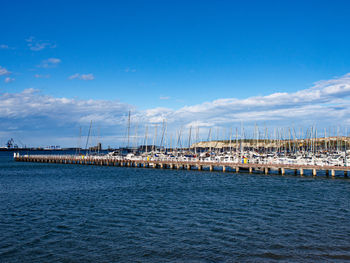 Sailboats moored at harbor against blue sky