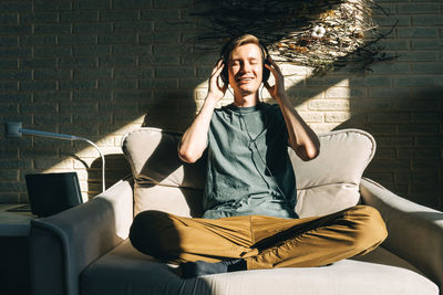 Full length of man meditating on sofa at home
