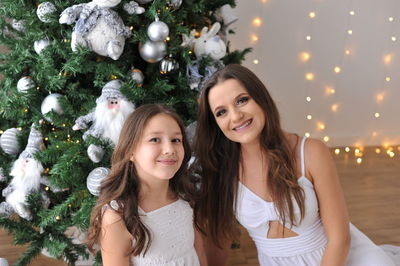 Portrait of young woman standing by christmas tree at home