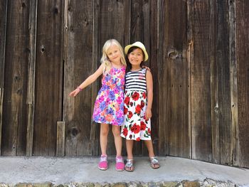 Portrait of smiling sisters standing against barn