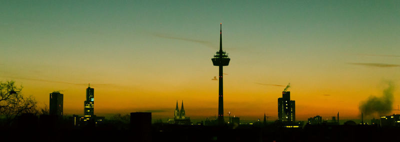 Communications tower in city against sky during sunset