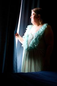 A beautiful middle-aged woman, in a lacy green nightgown, illuminated by window light.