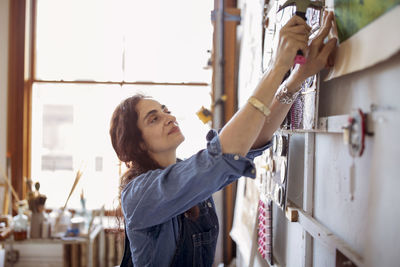 Artist hammering painting on wall in workshop