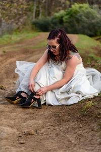 Young woman sitting on muddy road in wedding dress 