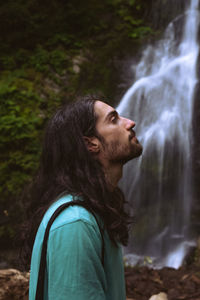 Side view of young man standing against waterfall