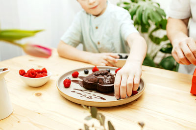 A boy decorates a heart-shaped chocolate cake for mother's day with fresh berries. valentine's day