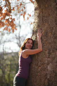 Portrait of woman with arms raised on tree trunk