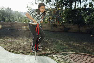 Girl jumping with pogo stick against sky at park during sunny day