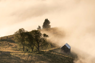 House on field by trees against sky