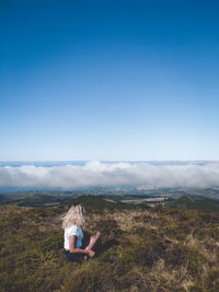 Woman sitting on landscape against sky