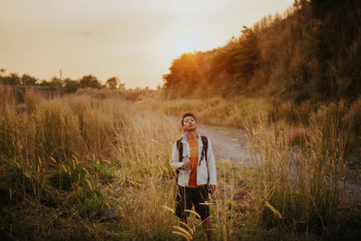 Rear view of man standing on field against sky during sunset