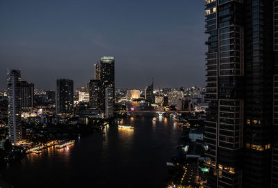 Illuminated buildings by river against sky in city at night