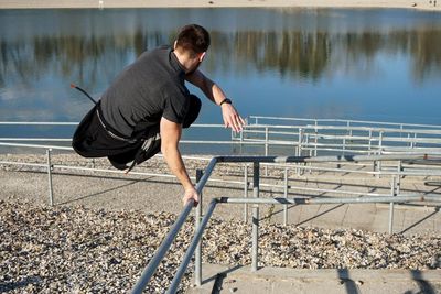 Rear view of man jumping over railing by lake