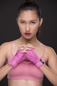 Portrait of young woman with wrapped hands clasped against black background