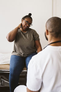 Mid adult woman consulting with male doctor about neck pain at medical clinic