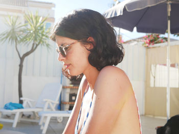 Side view of young woman wearing sunglasses sitting at poolside