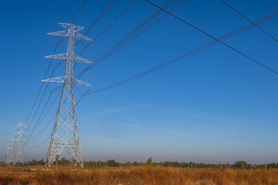 Electric pole and electric cable on the field in the countryside with blue sky.