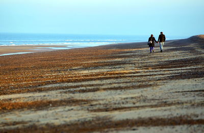 Rear view of couple walking at beach against clear blue sky