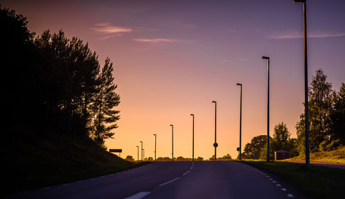 Road amidst silhouette trees against sky during sunset