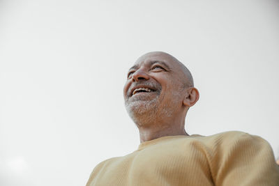 An elderly man gazes upwards with a broad smile, set against a clear sky