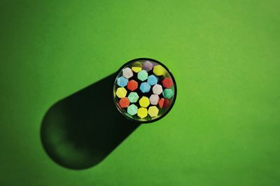 Directly above view of colorful chalks in glass with shadow on green background