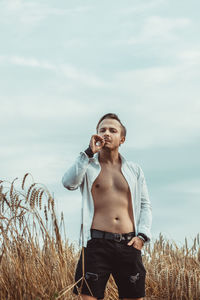 Young man smoking while standing on field against sky