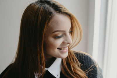 Positive young female with long red hair and perfect skin sincerely smiling and looking away