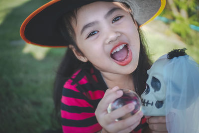 Portrait of girl wearing witch hat holding skull and crystal ball