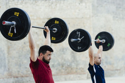 Two weightlifters lifting weights in an urban environment.