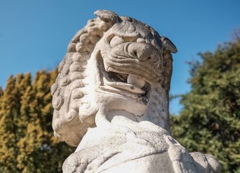 Low angle view of lion sculpture by trees against sky