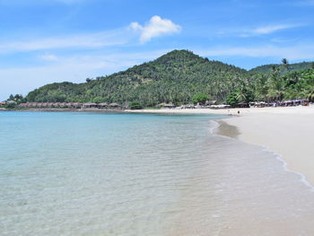 The sea beach with crystal water, big mountain, blue sky, and beach chairs with umbrella.