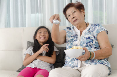 Grandmother with granddaughter watching tv while sitting on sofa at home